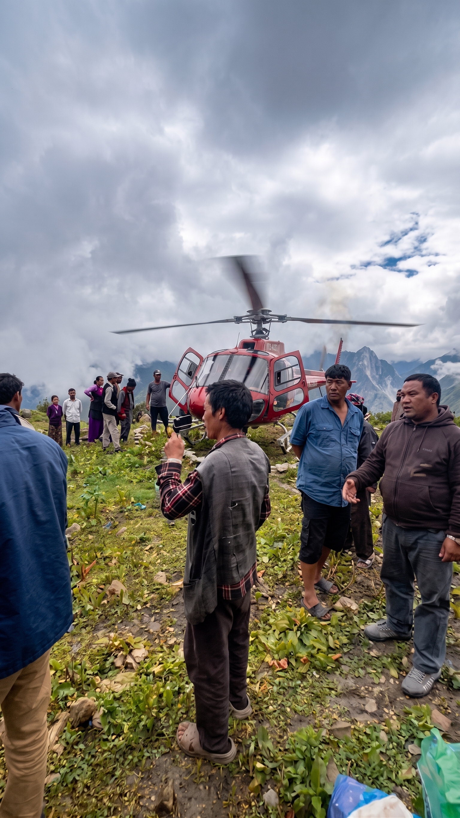 A helicopter on a hillside landing site in cloud, mountains behind, with villagers and REACT Responders unloading in the foreground